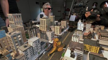 Movie still from “Jackass 4.5” (2022), directed by Jeff Tremaine – A man sitting in front of a model of a city; Extreme Wide shot, High angle
