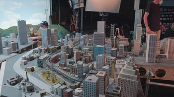 Movie still from “Jackass 4.5” (2022), directed by Jeff Tremaine – A model of a city with a train on the tracks; Extreme Wide shot, High angle