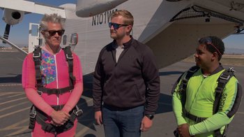 Movie still from “Jackass 4.5” (2022), directed by Jeff Tremaine – A man and two women standing in front of an airplane; Medium shot, Over the shoulder angle