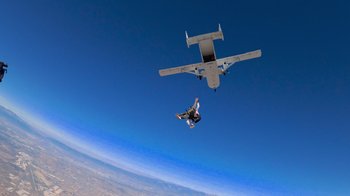 Movie still from “Jackass 4.5” (2022), directed by Jeff Tremaine – A person is parachuted into the sky by a plane; Extreme Wide shot, Overhead angle