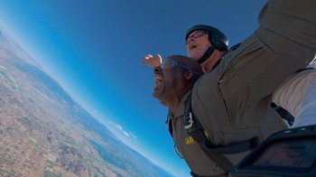 Movie still from “Jackass 4.5” (2022), directed by Jeff Tremaine – A man and a woman are skydiving in the sky; Medium shot, Low angle