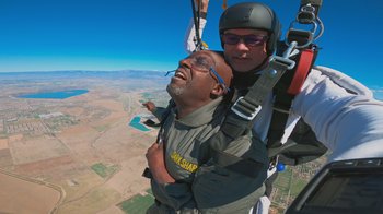Movie still from “Jackass 4.5” (2022), directed by Jeff Tremaine – A skydiver is holding a man up in the air; Medium shot, Low angle