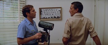 Movie still from “Jaws 2” (1978), directed by Jeannot Szwarc – Two men are talking in front of a picture of a group of people; Medium shot, Low angle