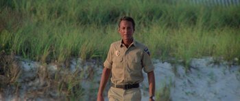 Movie still from “Jaws 2” (1978), directed by Jeannot Szwarc – A man in a uniform walking in front of a body of water; Medium shot, Low angle