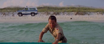 Movie still from “Jaws 2” (1978), directed by Jeannot Szwarc – A man in a uniform is on a surfboard in the ocean; Wide shot, Low angle