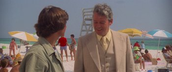 Movie still from “Jaws 2” (1978), directed by Jeannot Szwarc – A man in a suit and tie talking to a man in a suit and tie on the beach; Medium shot, Over the shoulder angle