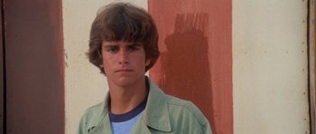 Movie still from “Jaws 2” (1978), directed by Jeannot Szwarc – A young man in a green jacket is standing in front of a red wall; Close Up shot, Low angle