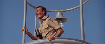 Movie still from “Jaws 2” (1978), directed by Jeannot Szwarc – A man in uniform holding onto a metal bell; Medium shot, Low angle