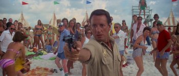 Movie still from “Jaws 2” (1978), directed by Jeannot Szwarc – A man holding a gun in front of a group of onlookers on the beach; Medium shot, Over the shoulder angle