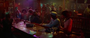 Movie still from “Jaws 2” (1978), directed by Jeannot Szwarc – A group of people sitting at a table in a bar; Wide shot, High angle