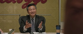 Movie still from “Jerry and Marge Go Large” (2022), directed by David Frankel – A man in a business suit sitting at a table; Medium shot, Over the shoulder angle