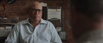 Movie still from “Jerry and Marge Go Large” (2022), directed by David Frankel – A bald man wearing glasses is standing in front of stacks of papers; Close Up shot, Over the shoulder angle