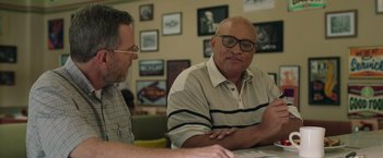 Movie still from “Jerry and Marge Go Large” (2022), directed by David Frankel – Two men sitting at a table looking at papers; Medium shot, Over the shoulder angle