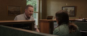 Movie still from “Jerry and Marge Go Large” (2022), directed by David Frankel – An older man and a young woman sitting at a desk; Medium shot, Over the shoulder angle