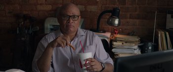 Movie still from “Jerry and Marge Go Large” (2022), directed by David Frankel – A man sitting at a desk with a drink in front of him; Medium shot, High angle