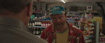 Movie still from “Jerry and Marge Go Large” (2022), directed by David Frankel – A man with a beard wearing a hat in a liquor store; Close Up shot, Over the shoulder angle