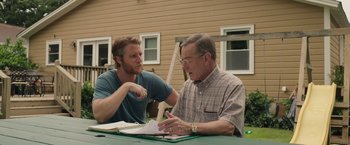 Movie still from “Jerry and Marge Go Large” (2022), directed by David Frankel – Two men are sitting at a table and one of the men is talking to another man; Medium shot, Over the shoulder angle