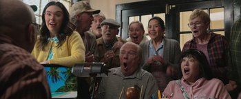 Movie still from “Jerry and Marge Go Large” (2022), directed by David Frankel – A group of people standing in a room; Medium shot, Low angle
