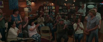 Movie still from “Jerry and Marge Go Large” (2022), directed by David Frankel – A group of people sitting in a room clapping; Wide shot, High angle