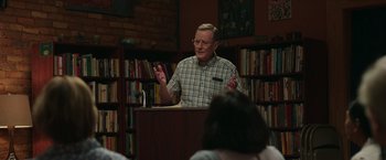 Movie still from “Jerry and Marge Go Large” (2022), directed by David Frankel – An older man is speaking in front of a group of people; Medium shot, Over the shoulder angle