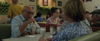 Movie still from “Jerry and Marge Go Large” (2022), directed by David Frankel – A group of people sitting at a table with drinks; Medium shot, Over the shoulder angle