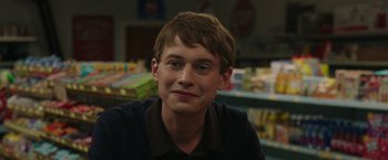 Movie still from “Jerry and Marge Go Large” (2022), directed by David Frankel – A young man sitting at a table in front of a shelf; Close Up shot, Over the shoulder angle