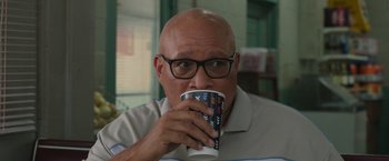 Movie still from “Jerry and Marge Go Large” (2022), directed by David Frankel – A bald man with glasses is drinking a cup of coffee; Close Up shot, Over the shoulder angle