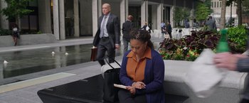 Movie still from “Jerry and Marge Go Large” (2022), directed by David Frankel – A woman sitting on a bench looking at a tablet; Wide shot, High angle