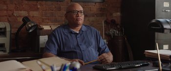 Movie still from “Jerry and Marge Go Large” (2022), directed by David Frankel – An older man sitting at a table with a pencil and a calculator; Medium shot, Low angle