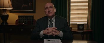 Movie still from “Jerry and Marge Go Large” (2022), directed by David Frankel – A man sitting at a table in front of papers; Medium shot, Low angle