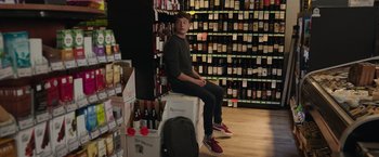 Movie still from “Jerry and Marge Go Large” (2022), directed by David Frankel – A man sitting on top of a box in a store; Wide shot, Low angle