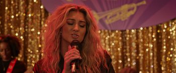 Movie still from “Jerry and Marge Go Large” (2022), directed by David Frankel – A woman holding a microphone in her hand; Close Up shot, Over the shoulder angle