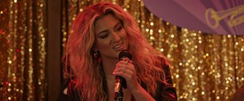 Movie still from “Jerry and Marge Go Large” (2022), directed by David Frankel – A beautiful woman holding a microphone in her hand; Close Up shot, Over the shoulder angle