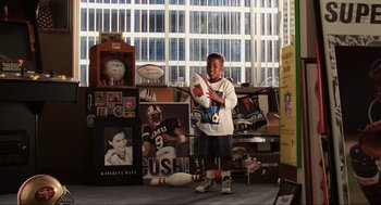 Movie still from “Jerry Maguire” (1996), directed by Cameron Crowe – A young boy holding a wii controller in a room full of sports memorabilia; Wide shot, High angle