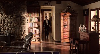 Movie still from “Jerry Maguire” (1996), directed by Cameron Crowe – A man in a suit walks through a doorway to a living room with bookshelves; Wide shot, Over the shoulder angle