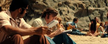 Movie still from “Jesus Revolution” (2023), directed by Brent McCorkle – A group of people sitting on the ground reading; Medium shot, Over the shoulder angle