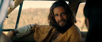 Movie still from “Jesus Revolution” (2023), directed by Brent McCorkle – A man with long hair and a beard sitting in a car; Close Up shot, Over the shoulder angle
