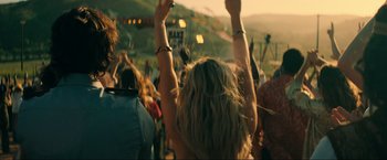 Movie still from “Jesus Revolution” (2023), directed by Brent McCorkle – A crowd of people at an outdoor event raising their hands; Medium shot, Over the shoulder angle