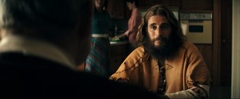 Movie still from “Jesus Revolution” (2023), directed by Brent McCorkle – A man with long hair and beard sitting in front of a kitchen; Medium shot, Over the shoulder angle
