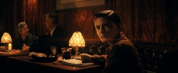 Movie still from “Jesus Revolution” (2023), directed by Brent McCorkle – A man sitting at a table with a pen in his hand; Medium shot, Over the shoulder angle