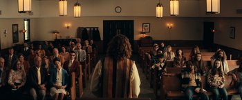 Movie still from “Jesus Revolution” (2023), directed by Brent McCorkle – A group of people sitting in a room with a person standing in front of them; Wide shot, Over the shoulder angle