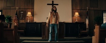 Movie still from “Jesus Revolution” (2023), directed by Brent McCorkle – A man standing in front of a cross in a church; Wide shot, Low angle