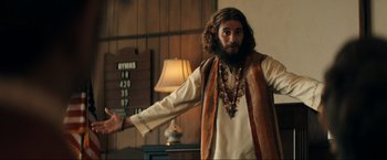 Movie still from “Jesus Revolution” (2023), directed by Brent McCorkle – A man with long hair and a beard wearing a long vest; Medium shot, Over the shoulder angle