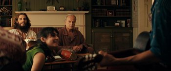 Movie still from “Jesus Revolution” (2023), directed by Brent McCorkle – An older man sitting in front of a fireplace; Medium shot, Over the shoulder angle