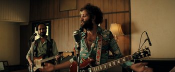 Movie still from “Jesus Revolution” (2023), directed by Brent McCorkle – A man holding a microphone while playing a guitar; Medium shot, Low angle