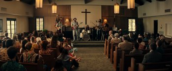 Movie still from “Jesus Revolution” (2023), directed by Brent McCorkle – A group of people sitting in front of a cross; Wide shot, High angle