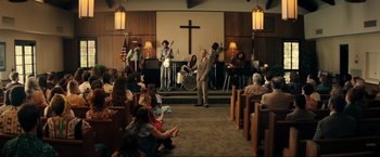 Movie still from “Jesus Revolution” (2023), directed by Brent McCorkle – A group of people sitting in front of a cross; Wide shot, High angle