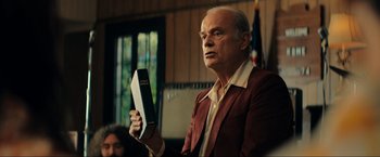 Movie still from “Jesus Revolution” (2023), directed by Brent McCorkle – An older man holding a bible in front of an american flag; Medium shot, Low angle