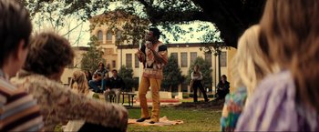 Movie still from “Jesus Revolution” (2023), directed by Brent McCorkle – A man standing on the grass holding a microphone; Wide shot, Over the shoulder angle