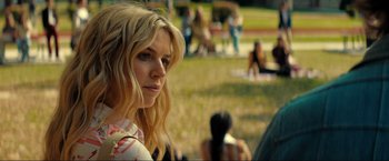 Movie still from “Jesus Revolution” (2023), directed by Brent McCorkle – A woman sitting in the grass with people in the background; Close Up shot, Over the shoulder angle